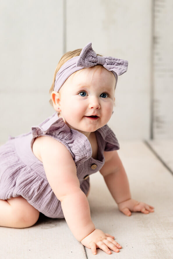 Cute baby with purple bow looks at her mom off camera.