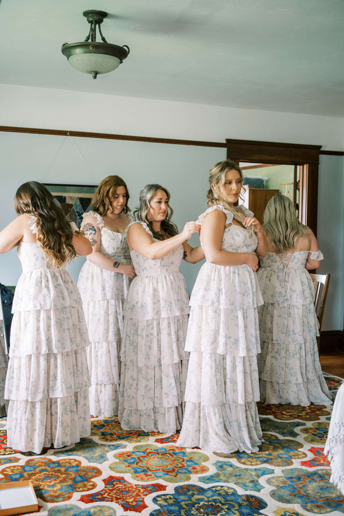 A group of brides maids help each other zip up their dresses before a wedding.