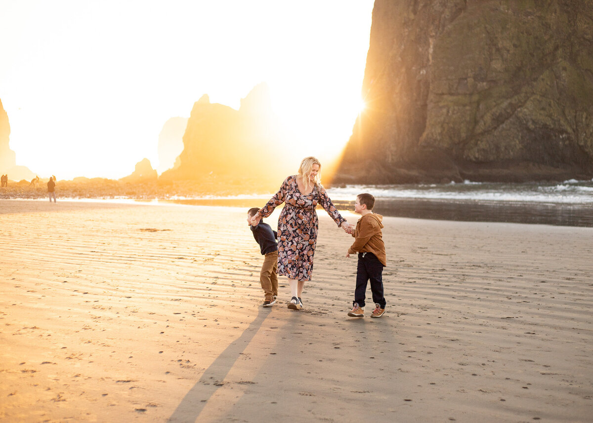 A mother with her young sons holding hands at sunset in front of Haystack Rock by Cannon Beach photographer Jaime Bugbee.