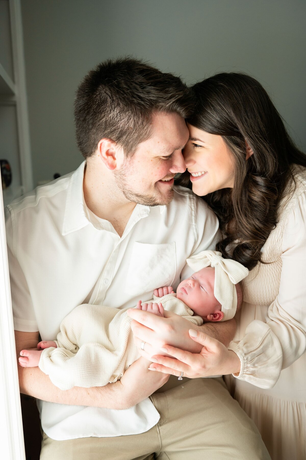mom and dad looking t each other smiling while newborn girl sleeps