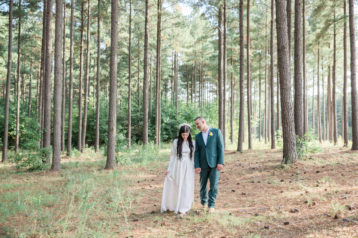 A wedding couple holding hands and walking down a path through long, skinny trees