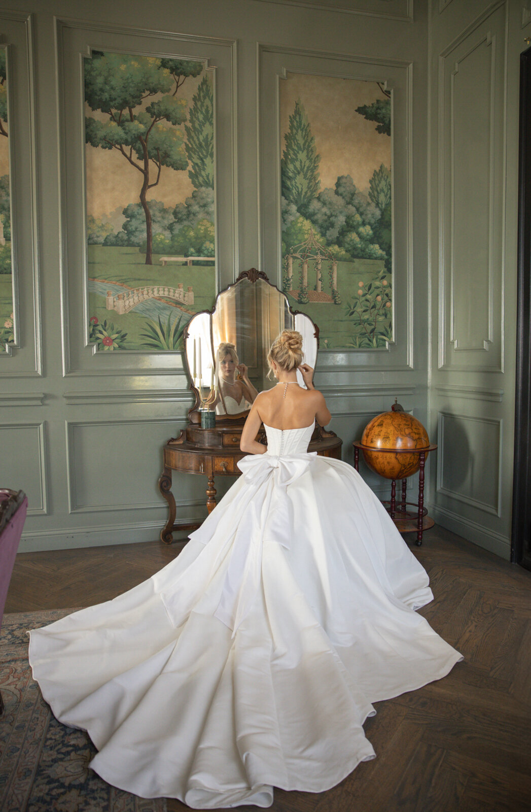 Bridal portrait at The Mason with the bride looking at herself in the mirror, showcasing a long train with a bow on her gown