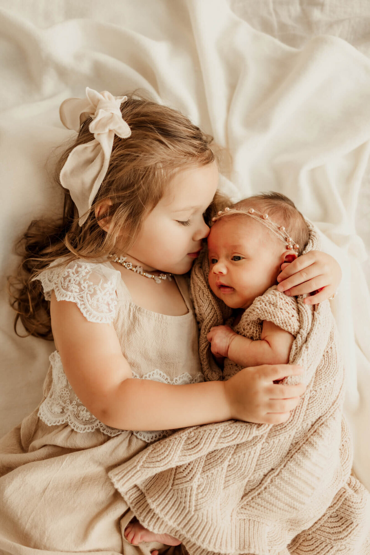 Older sister snuggles her newborn baby sister while laying down for a newborn photo session in Tulsa, Oklahoma.