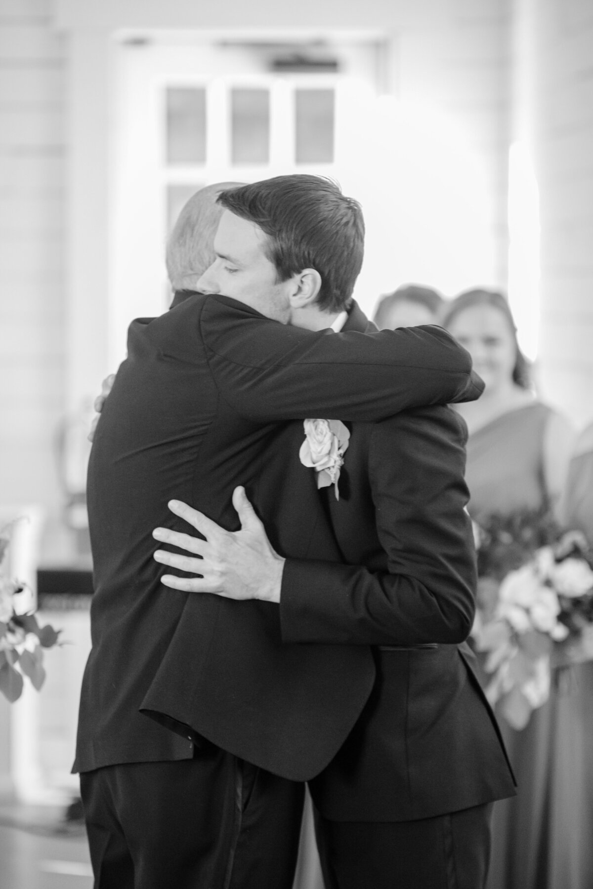 groom hugs bride's father in black and white captured by wedding photographer in Texas