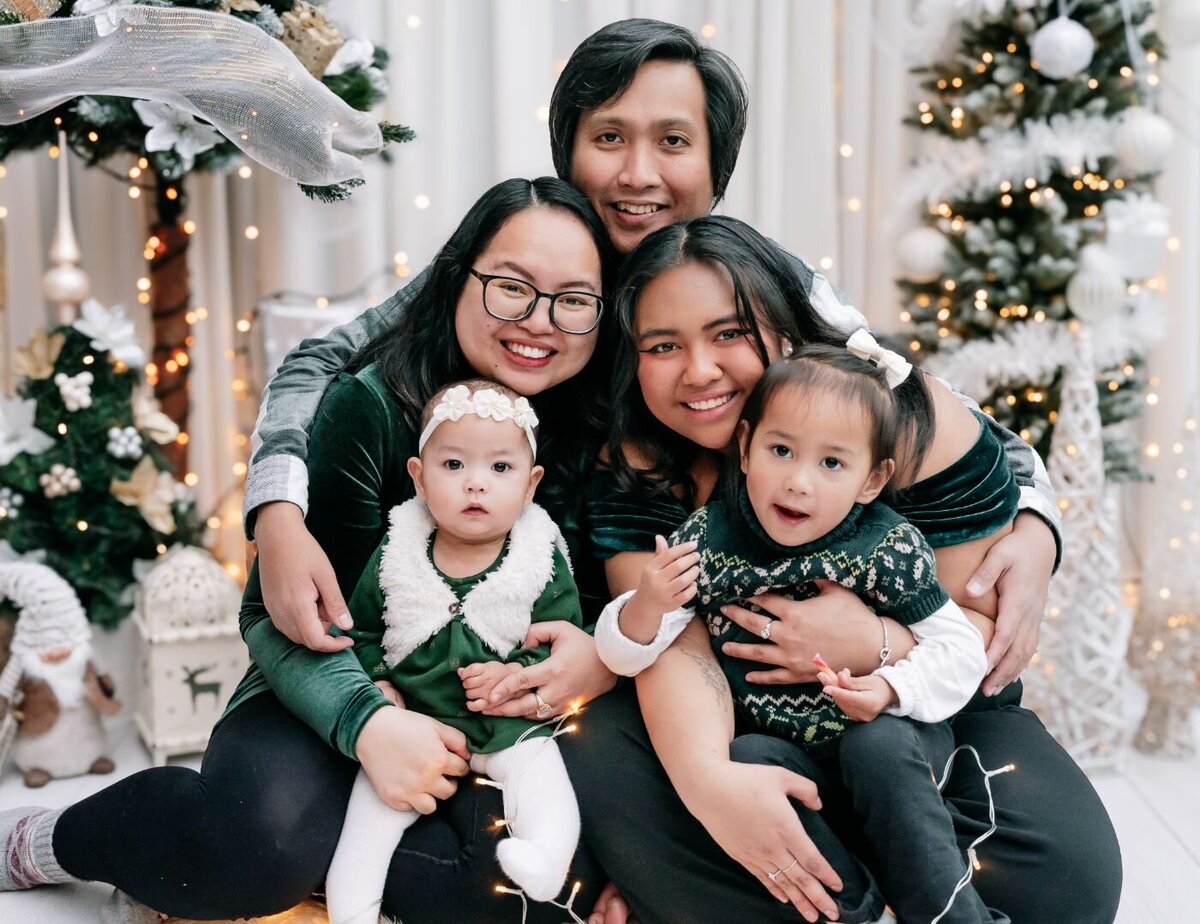 Parents with two young daughters in matching green outfits posing in a festive Christmas studio