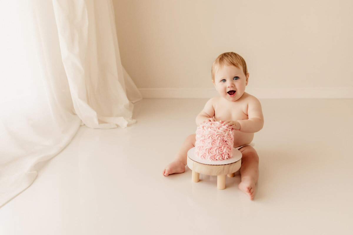 Cake smash photo of a girl with a pink icing cake on a white floor in OKC.