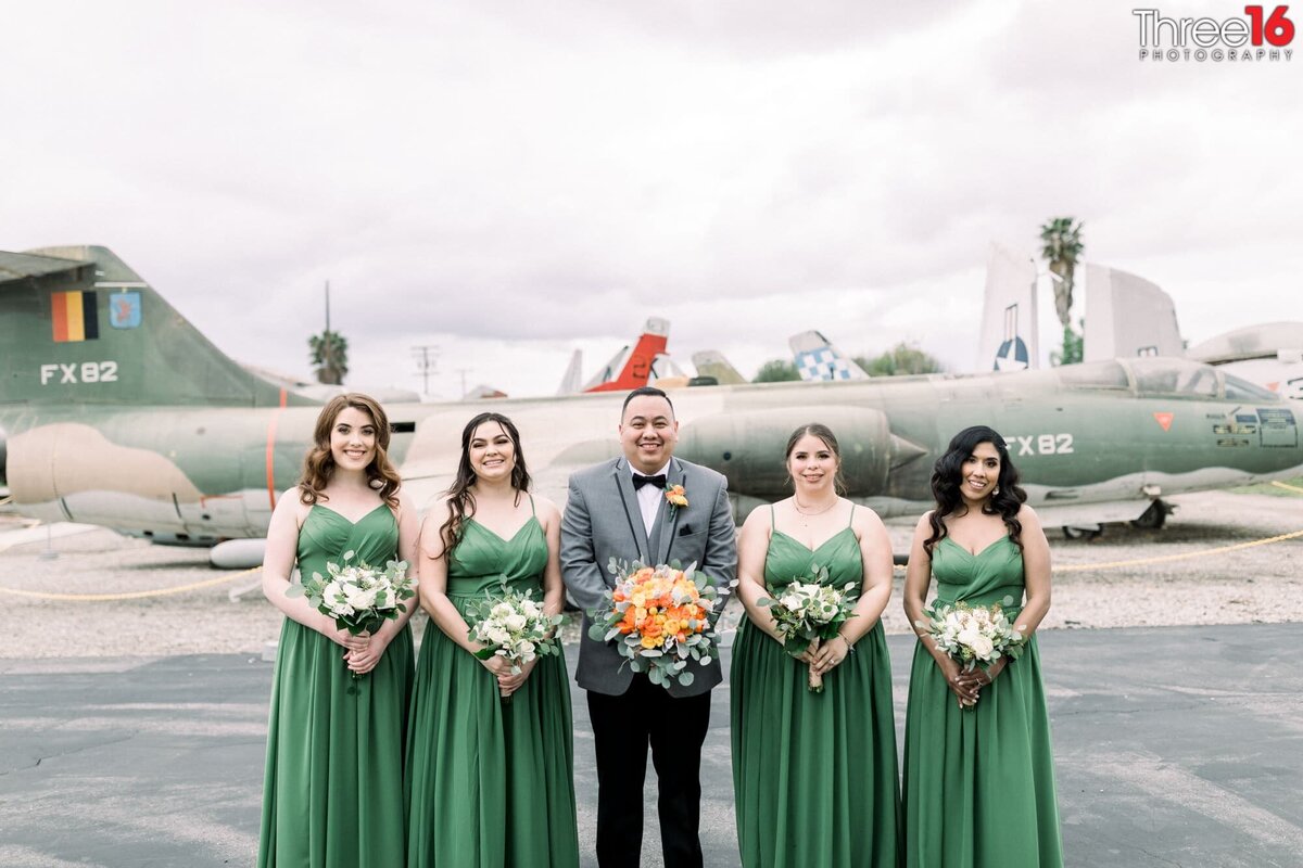 Groom holds his Bride's bouquet as he poses with the Bridesmaids