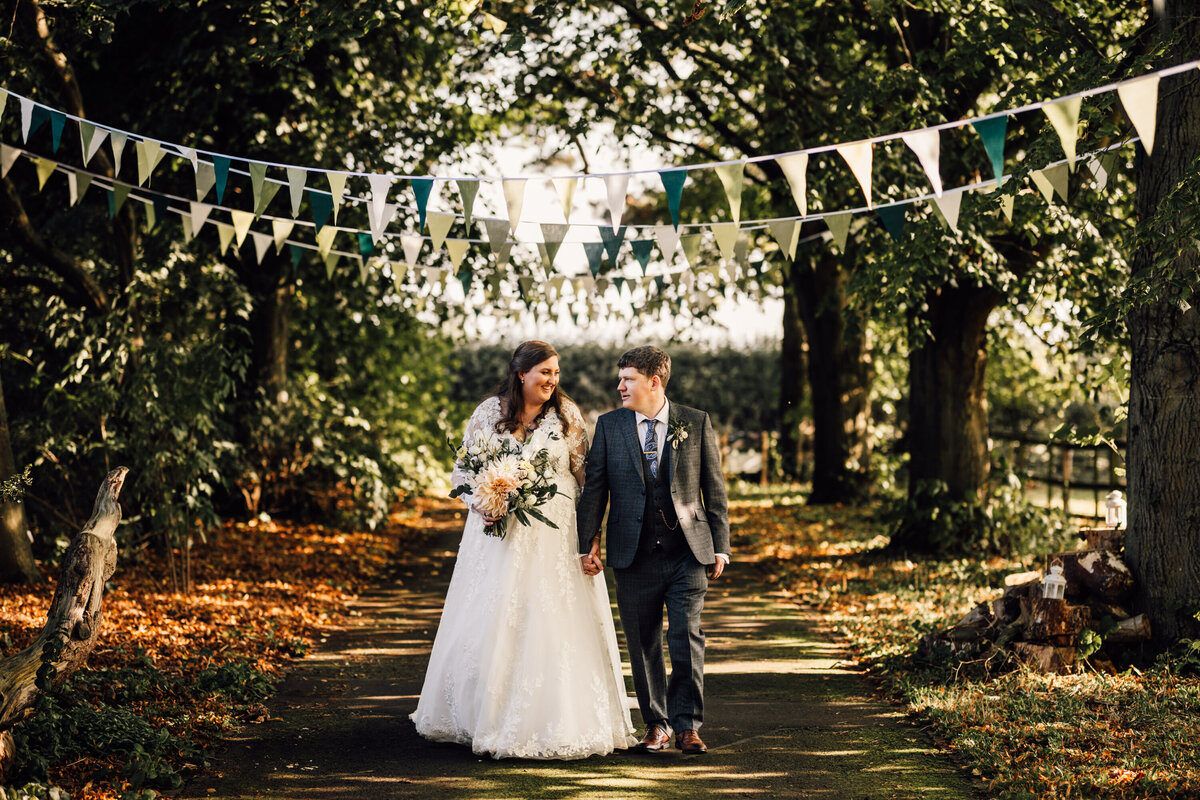 Bride and groom strolling down tree-lined path with flag banners