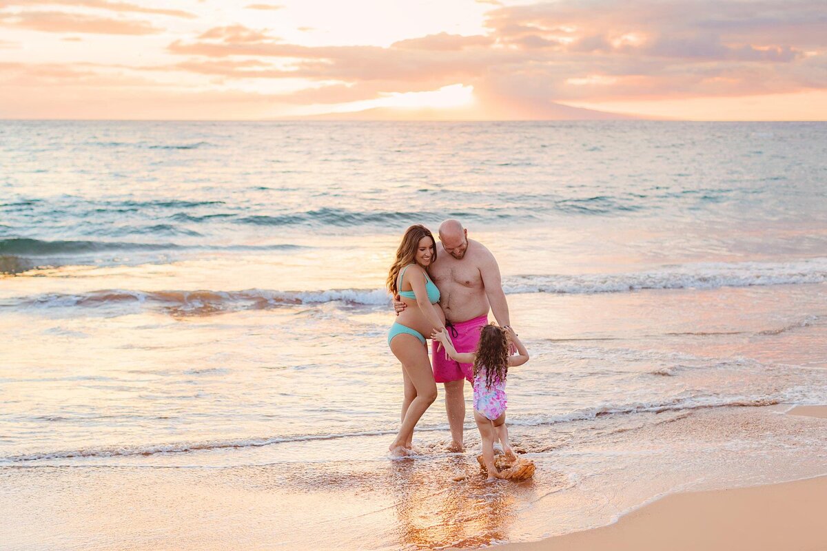Cute family Maui portrait with pregnant mom and dad wearing colorful swim trunks on the beach