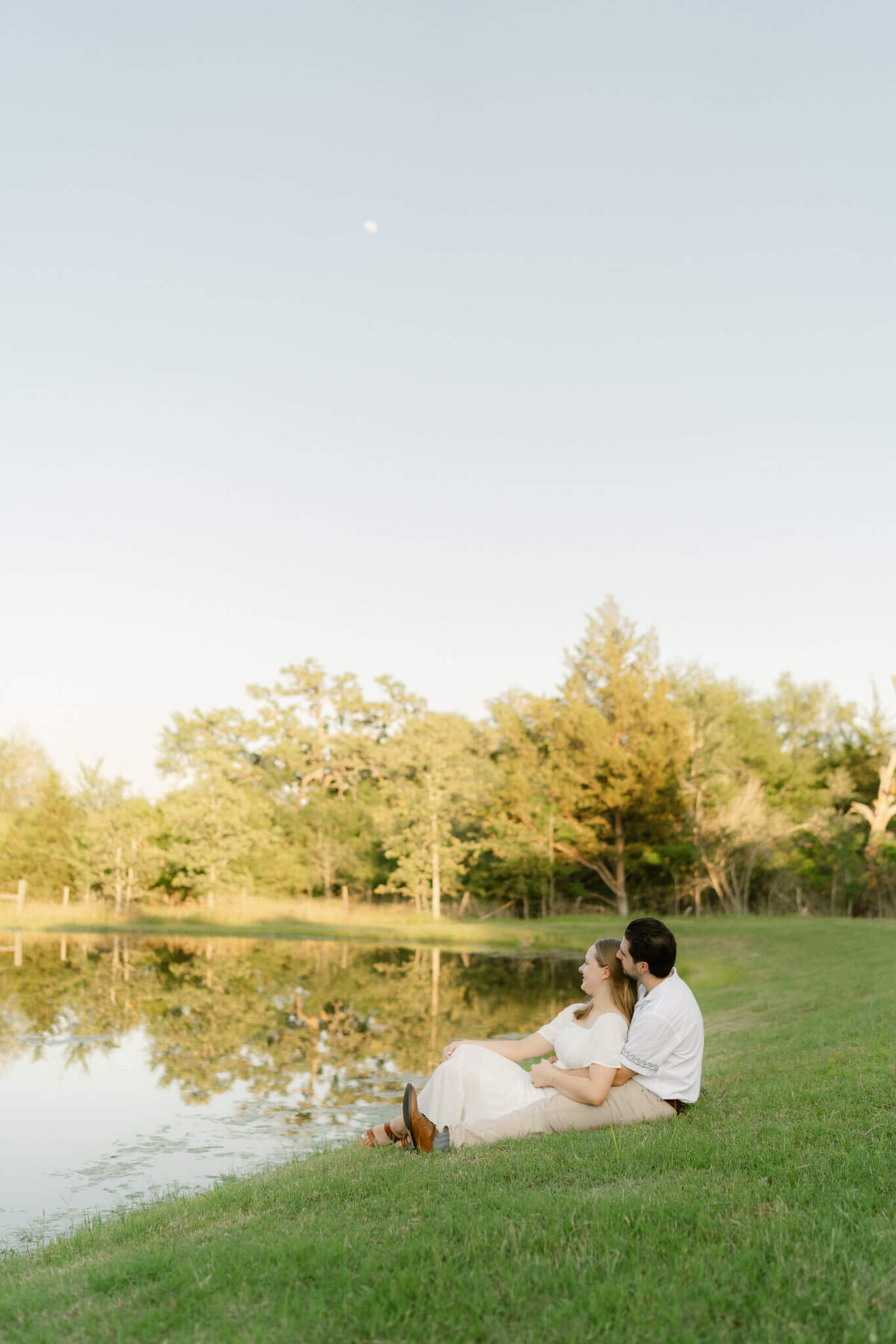 a couple sitting at a pond near sunset