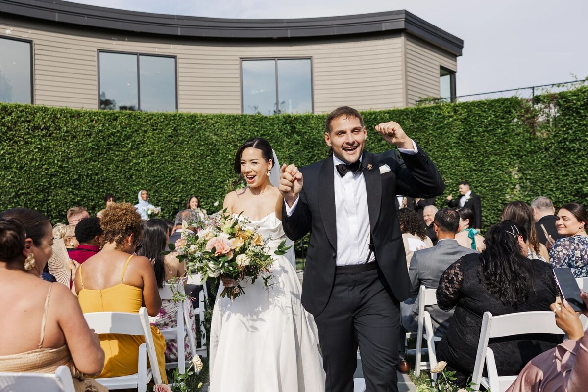 Bride and groom cheer while they walk down the aisle during their outdoor ceremony at The Roundhouse
