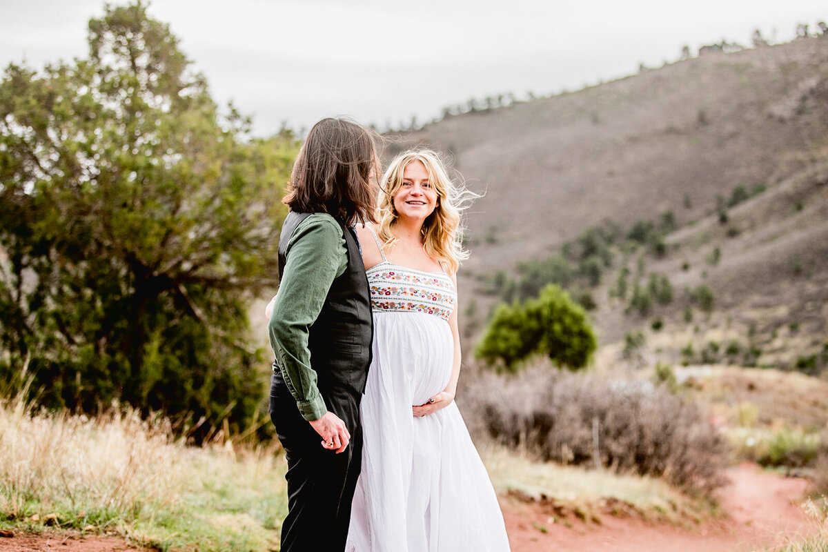 a pregnant woman in white holds her baby bump as her husband looks at her in lyons, colorado