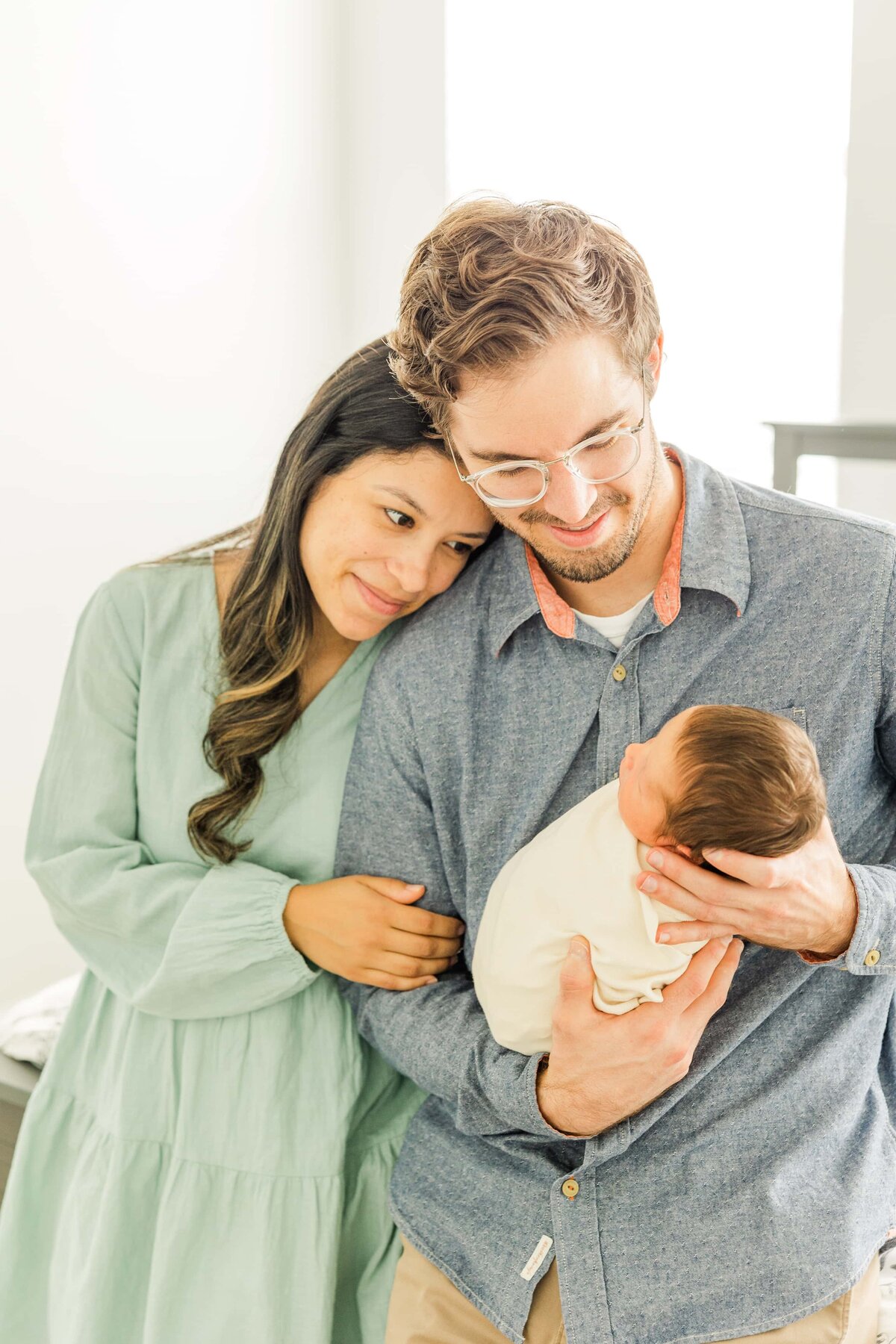 Mom rest head on dads shoulder while both look at their newborn in Windsor,, CO