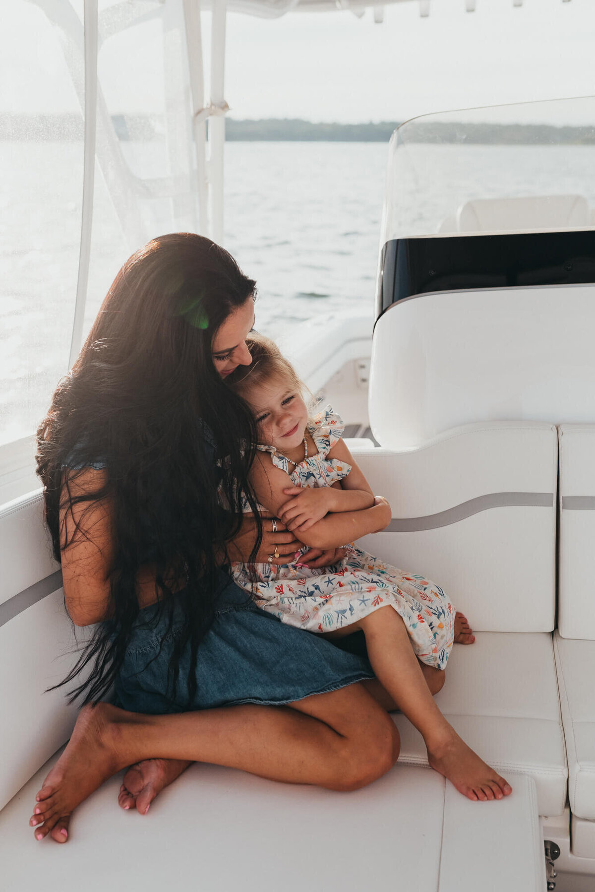 A young mother with long black hair snuggles her daughter on their family boat at sunset