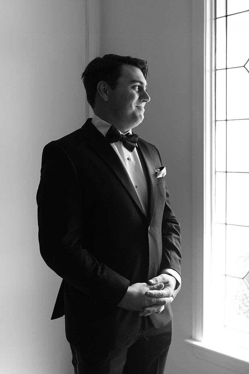 groom with hands together looking out the window
