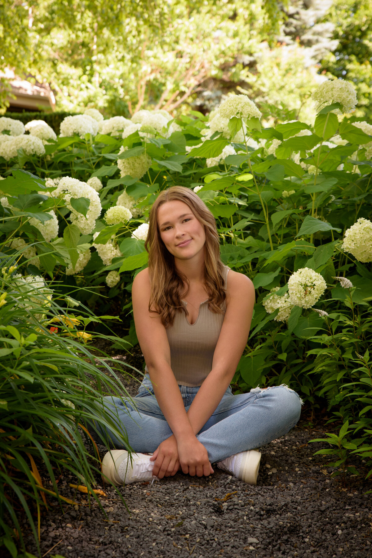 Luxemburg Casco High School senior girl wearing ripped jeans and a tan shirt sitting in flowers at the Green Bay Botanical Gardens in Green Bay, Wisconsin