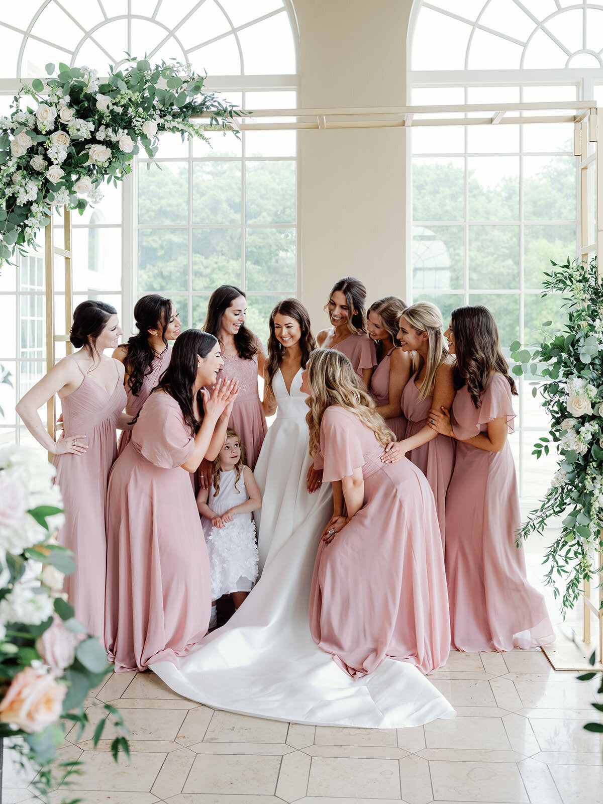 Brid is surrounded by bridesmaids wearing blush colored dresses