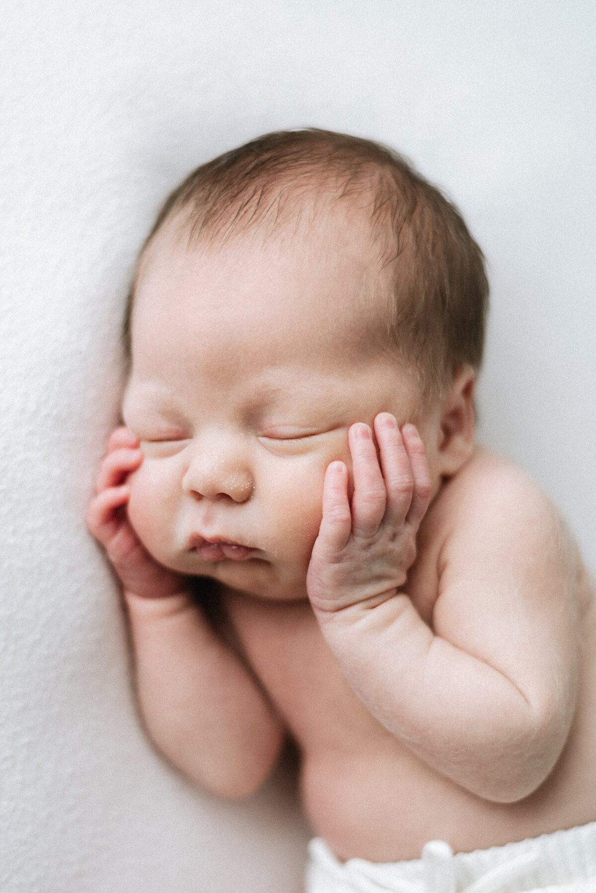 newborn baby holding hands on their face whilst sleeping at a west sussex newborn photoshoot