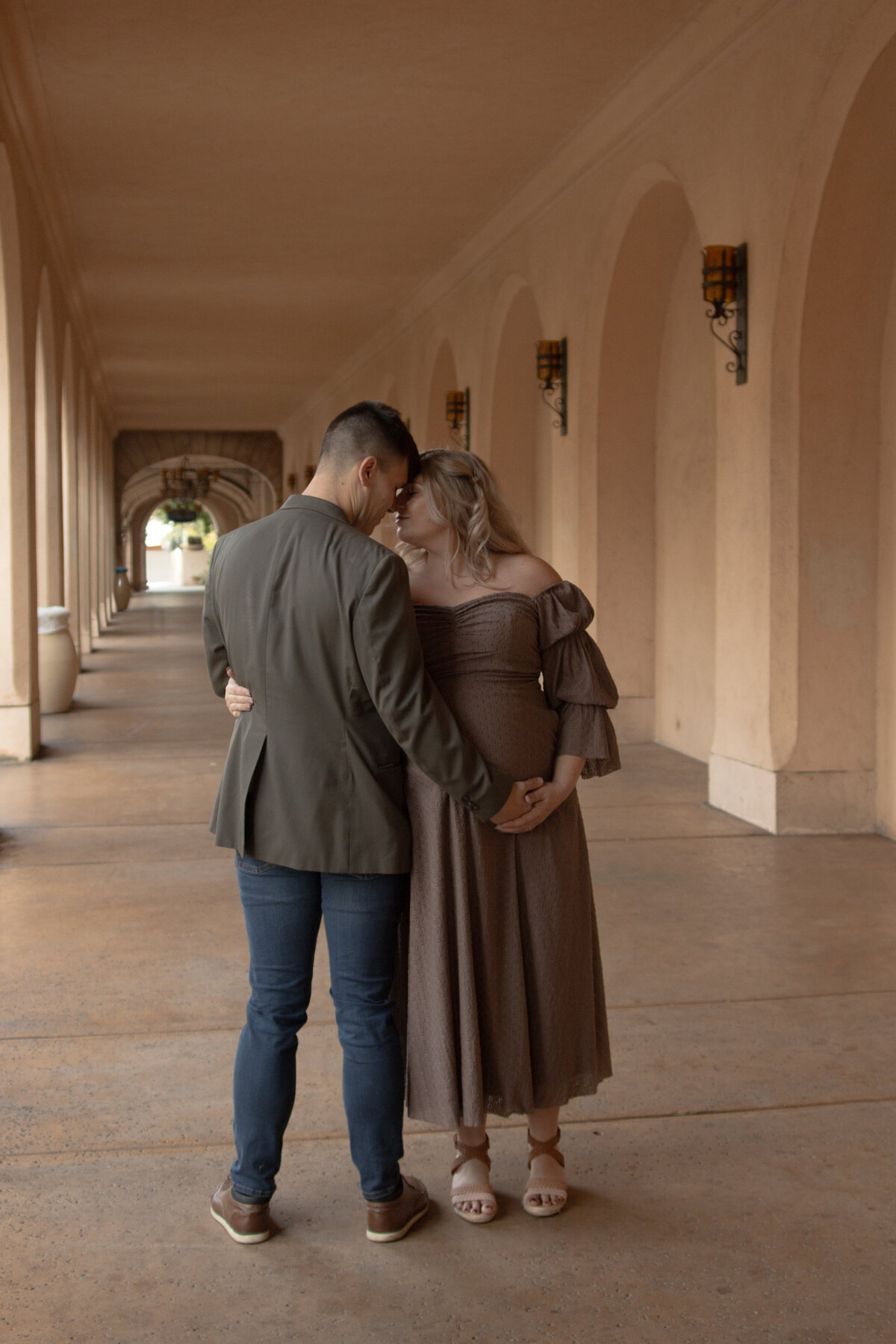 expecting mom and dad having an intimate moment in the arches of balboa park