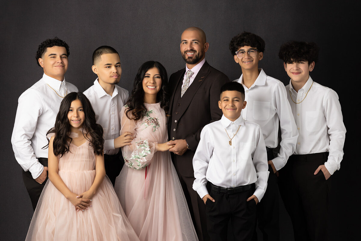 A beautiful family captured by a Dallas family photographer, smiling in coordinated white shirts and elegant attire, set against a neutral background.