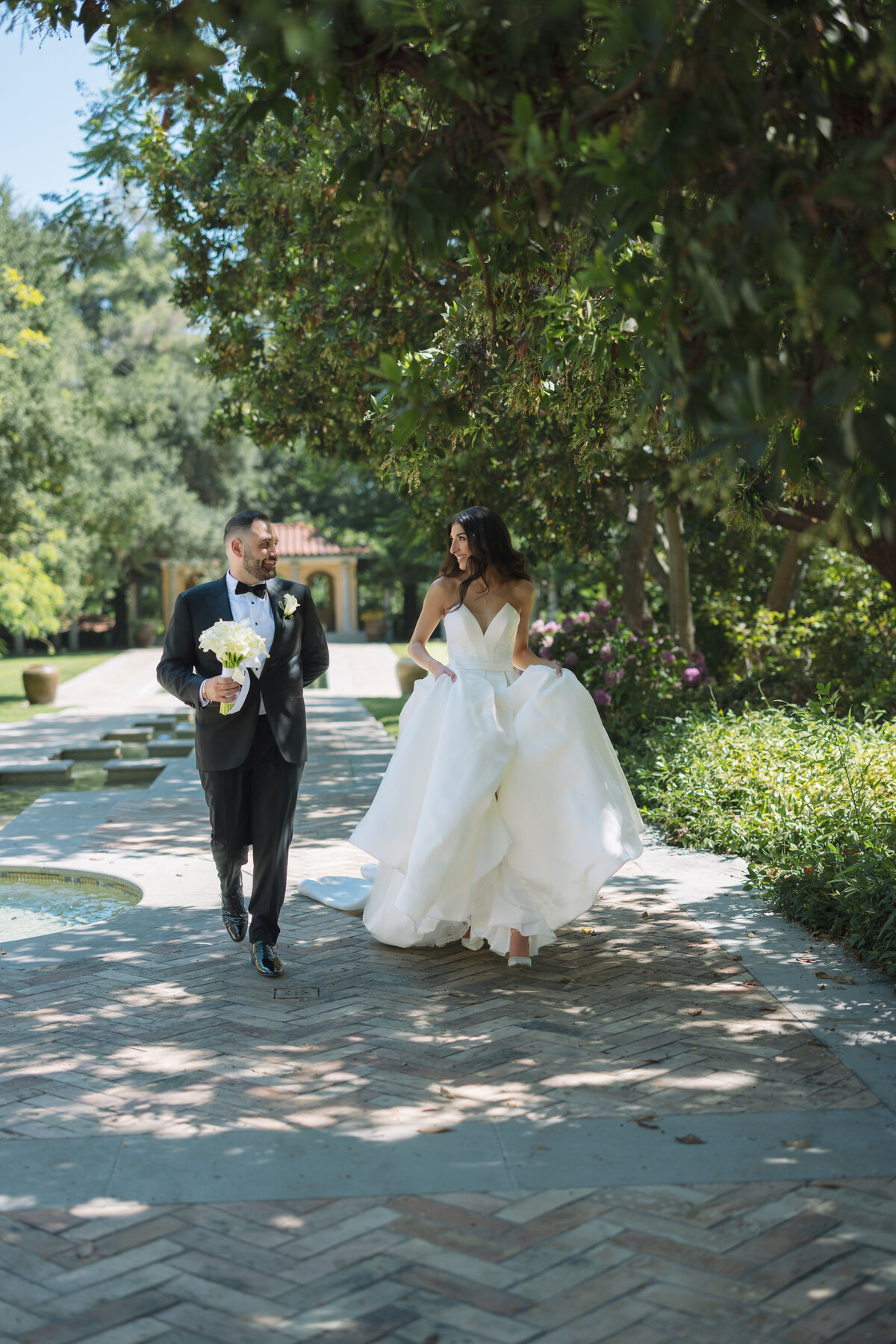 Bride and Groom walking towards the camera. The scene behind is of a Mediterrean Vila