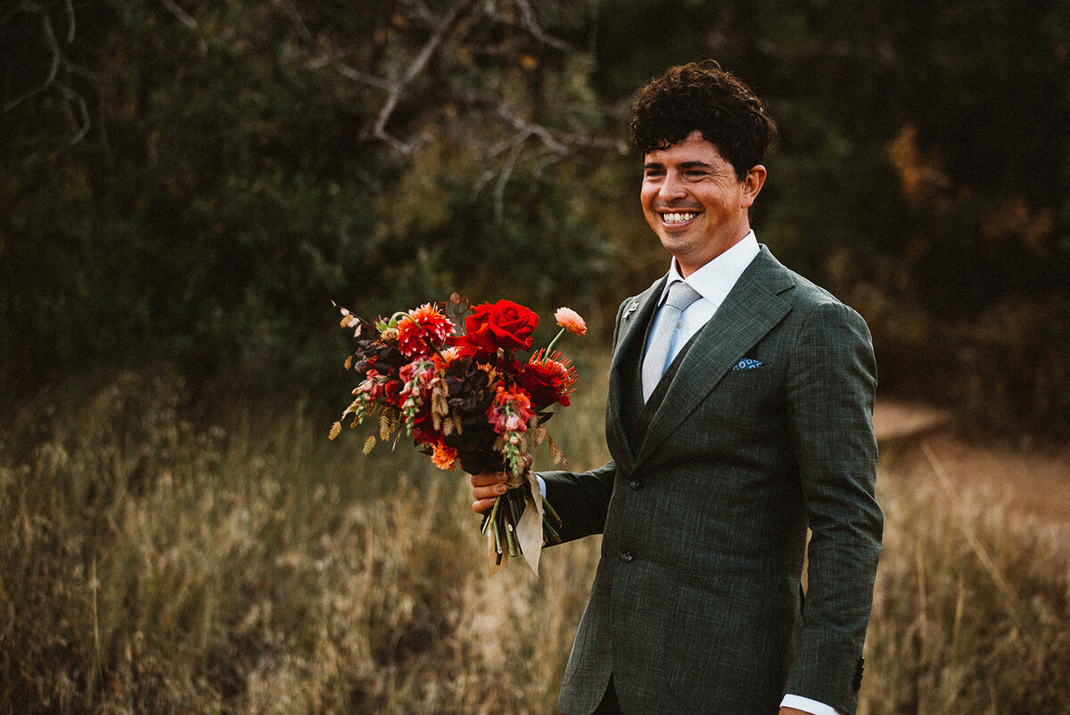 groom smiles and holds wedding flowers