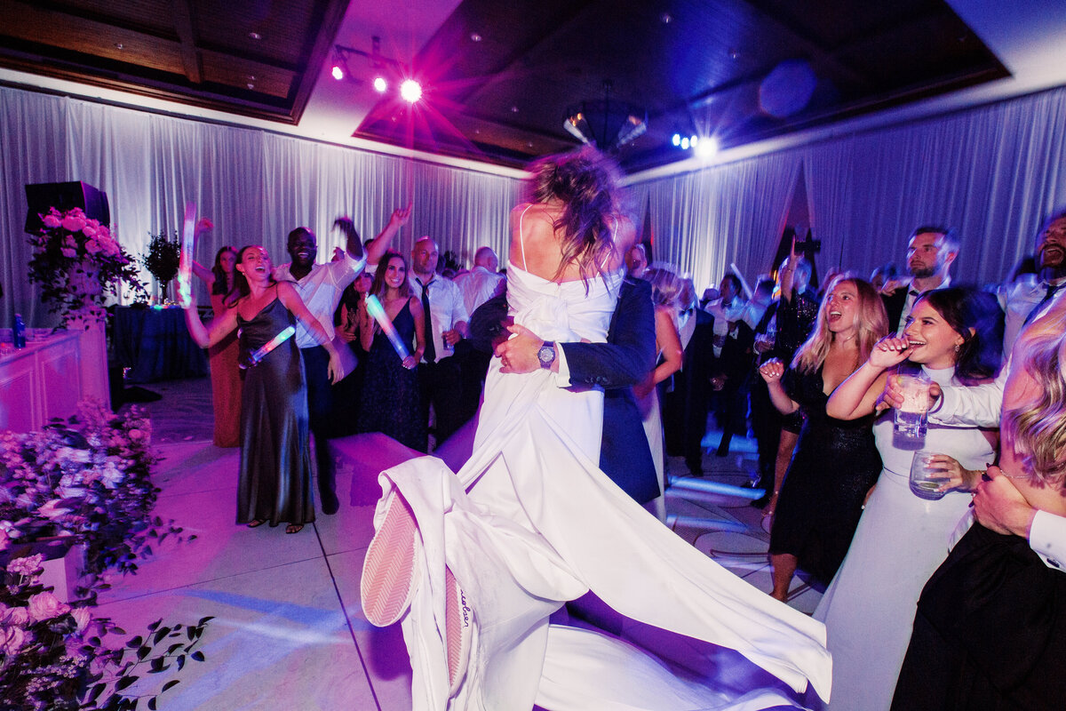 The newlyweds embrace on the dance floor as friends and family cheer, capturing a lively and joyous wedding celebration.