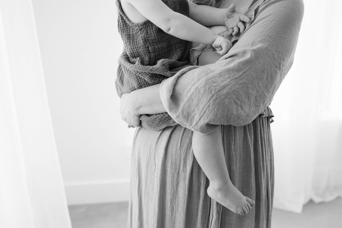 stunning black and white portrait of mom holding her daughter on top of her growing baby bump