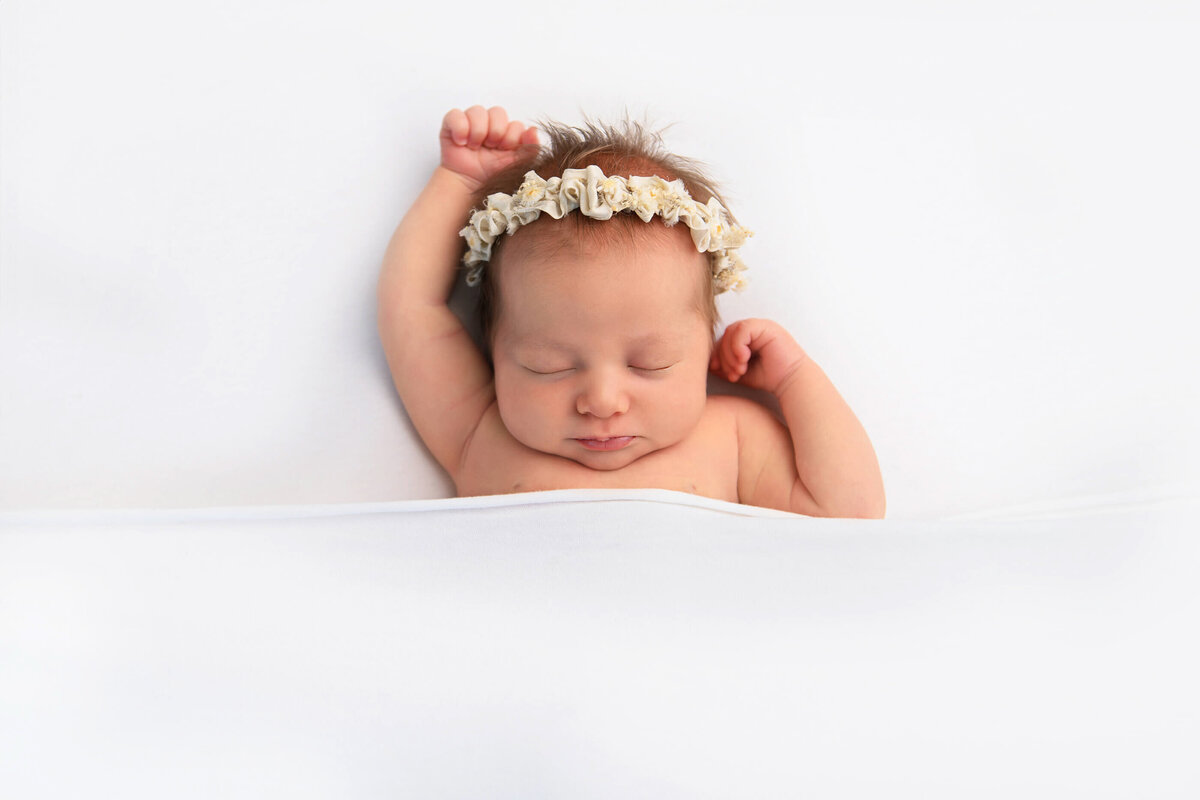 newborn girl wearing a headband laying on a white background for her newborn photography session in Burlington Ontario 