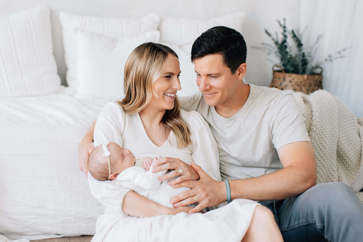 mom and dad sitting in front of the bed with newborn in mom's arms