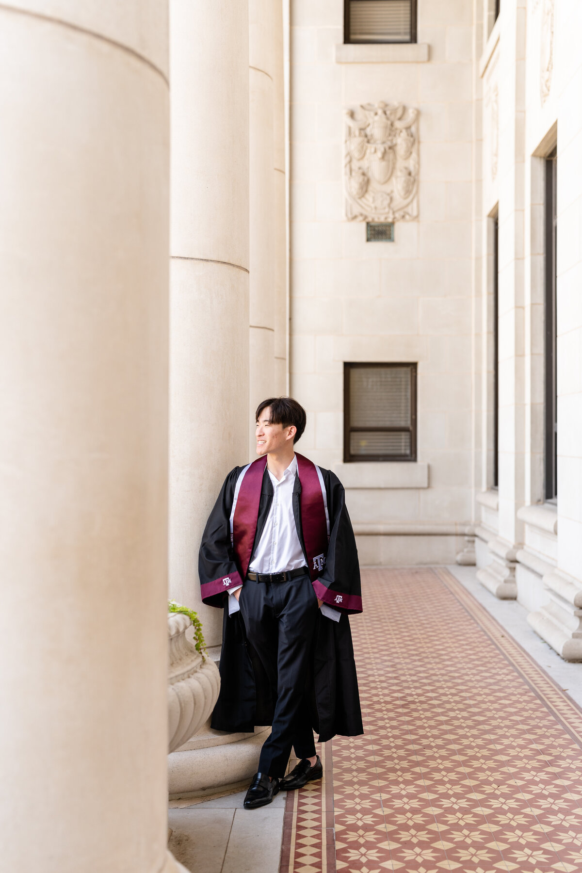 Texas A&M senior guy wearing gown and Aggie stole and looking away while leaning against column at Administration Building