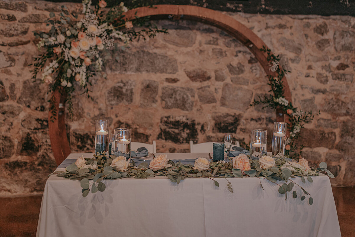 Bride and grooms table with arch and stonewall as a backdrop