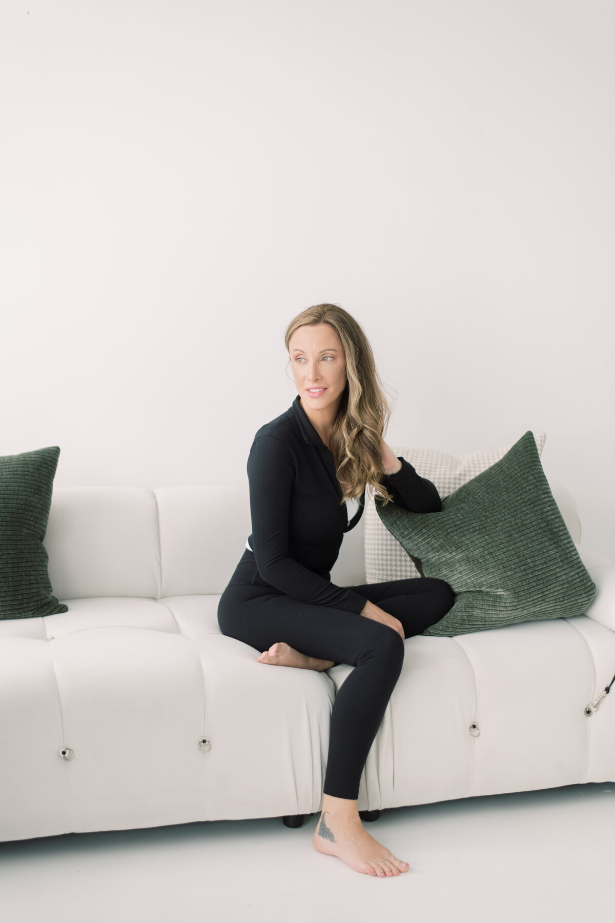 Casual seated branding portrait on white sofa with green pillows, relaxed and confident
