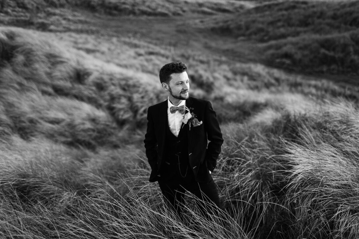 Black and white portrait of a groom on top of sand dunes in Northumberland