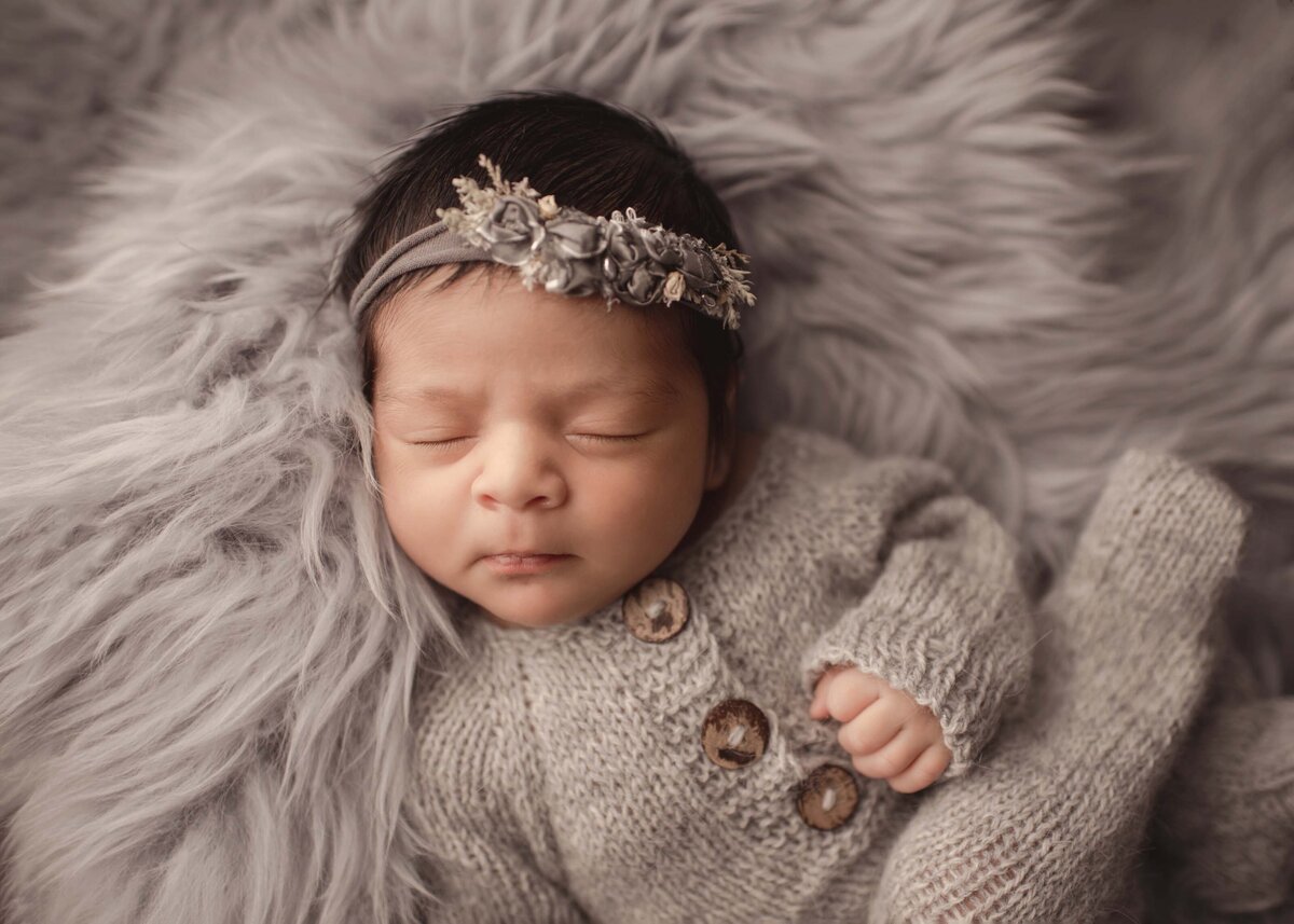 Newborn baby sleeping on grey flokati wearing grey knit outfit with coordinating floral headband