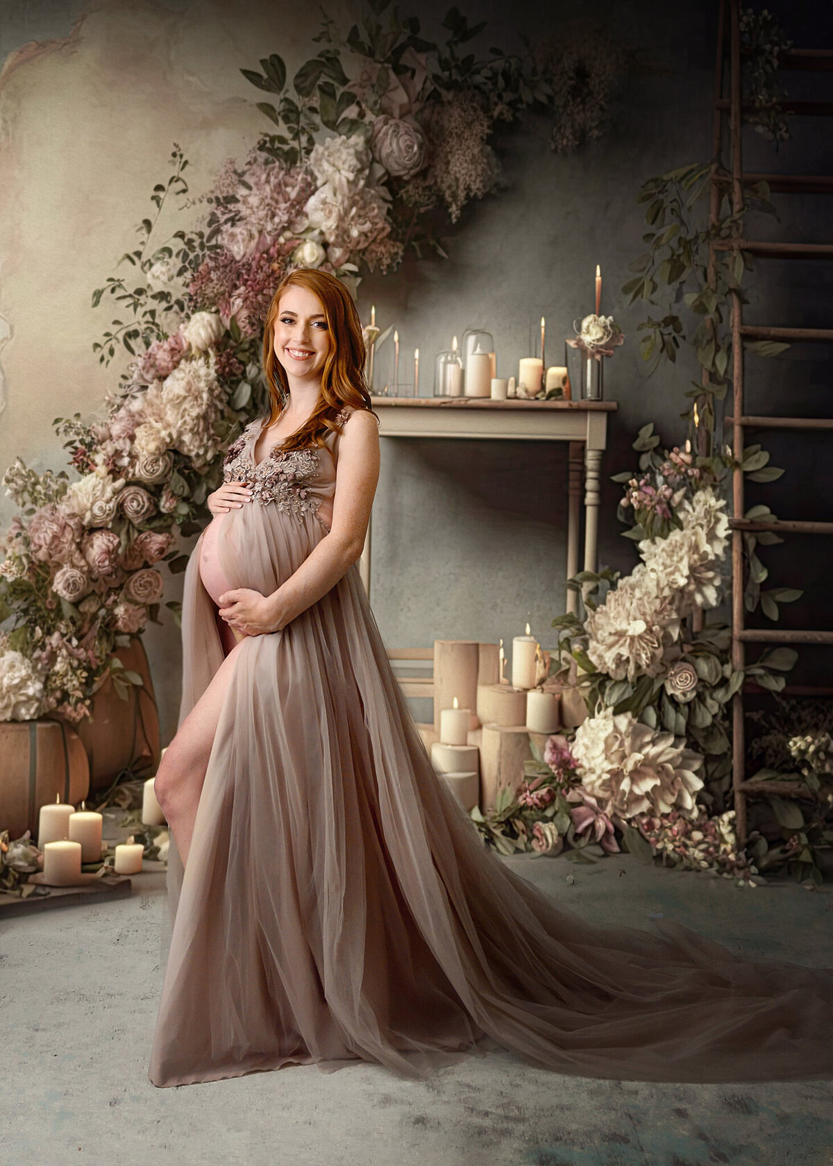 Beautiful red haired pregnant woman in a dark tan neutral gown standing in room with fireplace, wooden ladder, candles and floral arrangements