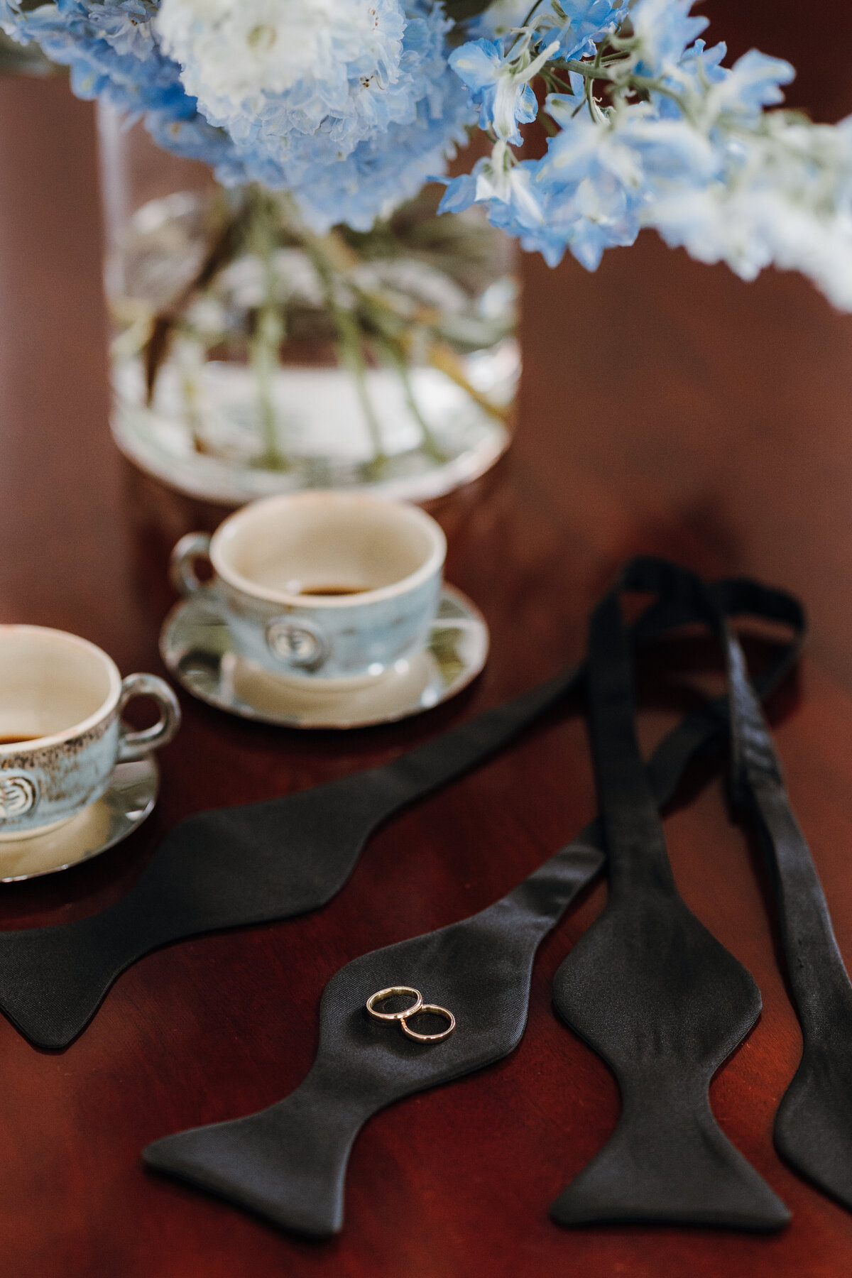 The grooms' bow ties, cups of coffee, and their gold wedding bands.