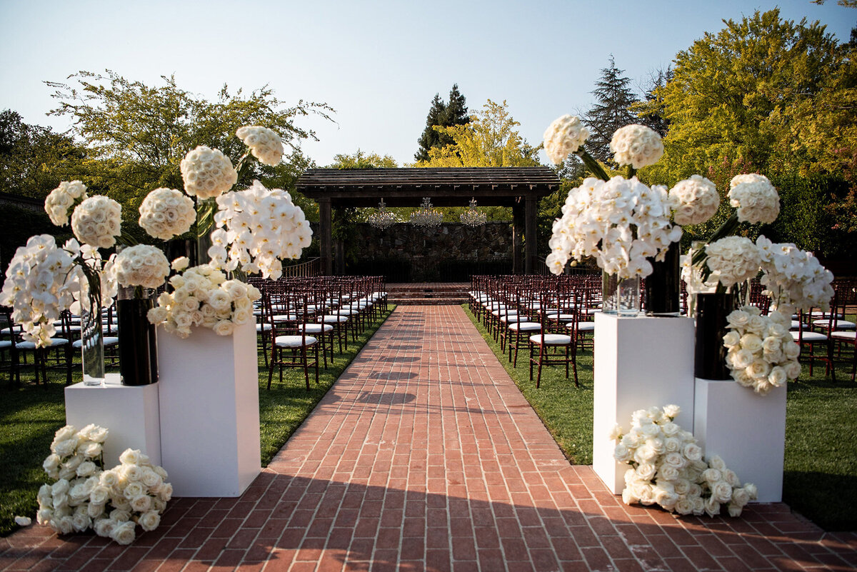 San Francisco Bay Area wedding photographer captures elegant ceremony setup with white hydrangea arrangements and brick aisle leading to pergola at Estate Yountville in Napa Valley