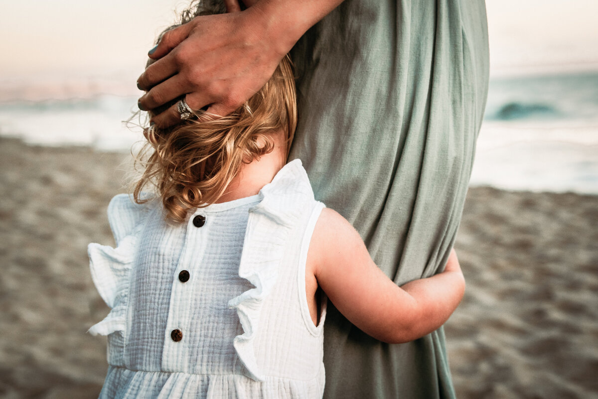 Toddler hugs mother's leg on beach