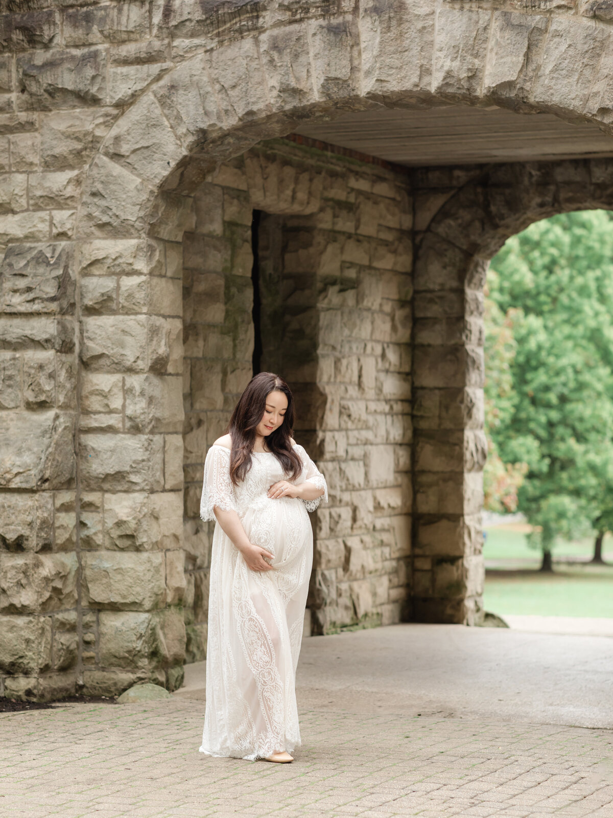 pregnant mother in white lace gown holding belly for maternity portraits 