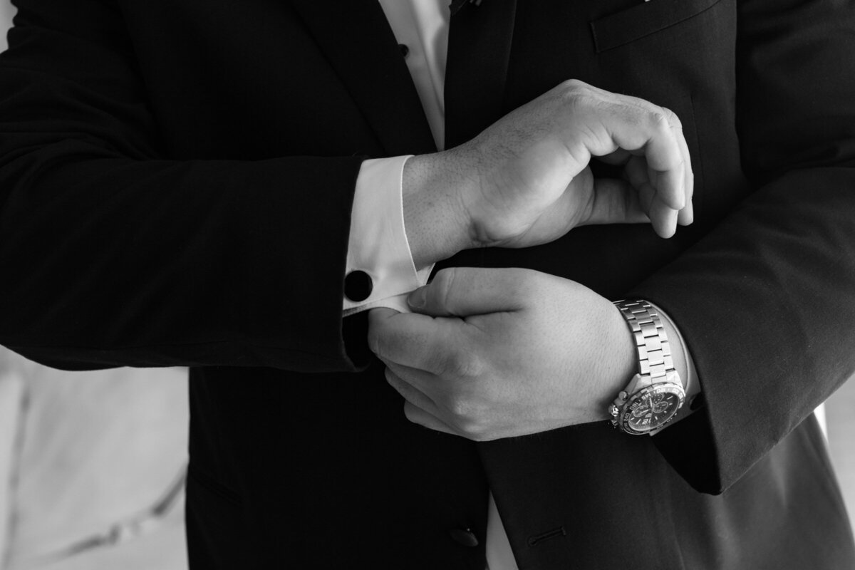 black and white close up of the groom’s hands fastening cufflinks at The Adolphus in Dallas, emphasizing refined wedding preparation details.