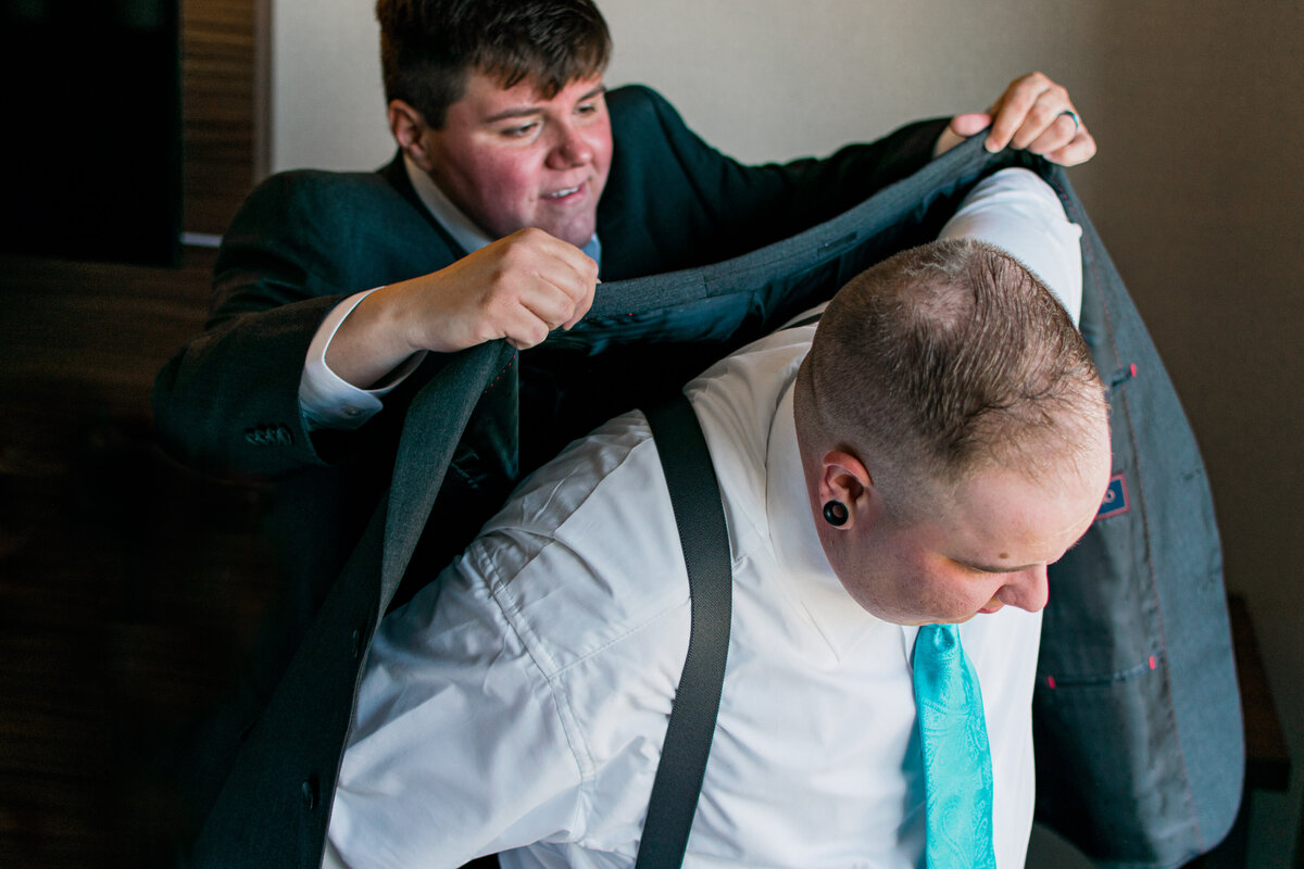 Groom having their suit jacket put on by a groomsman