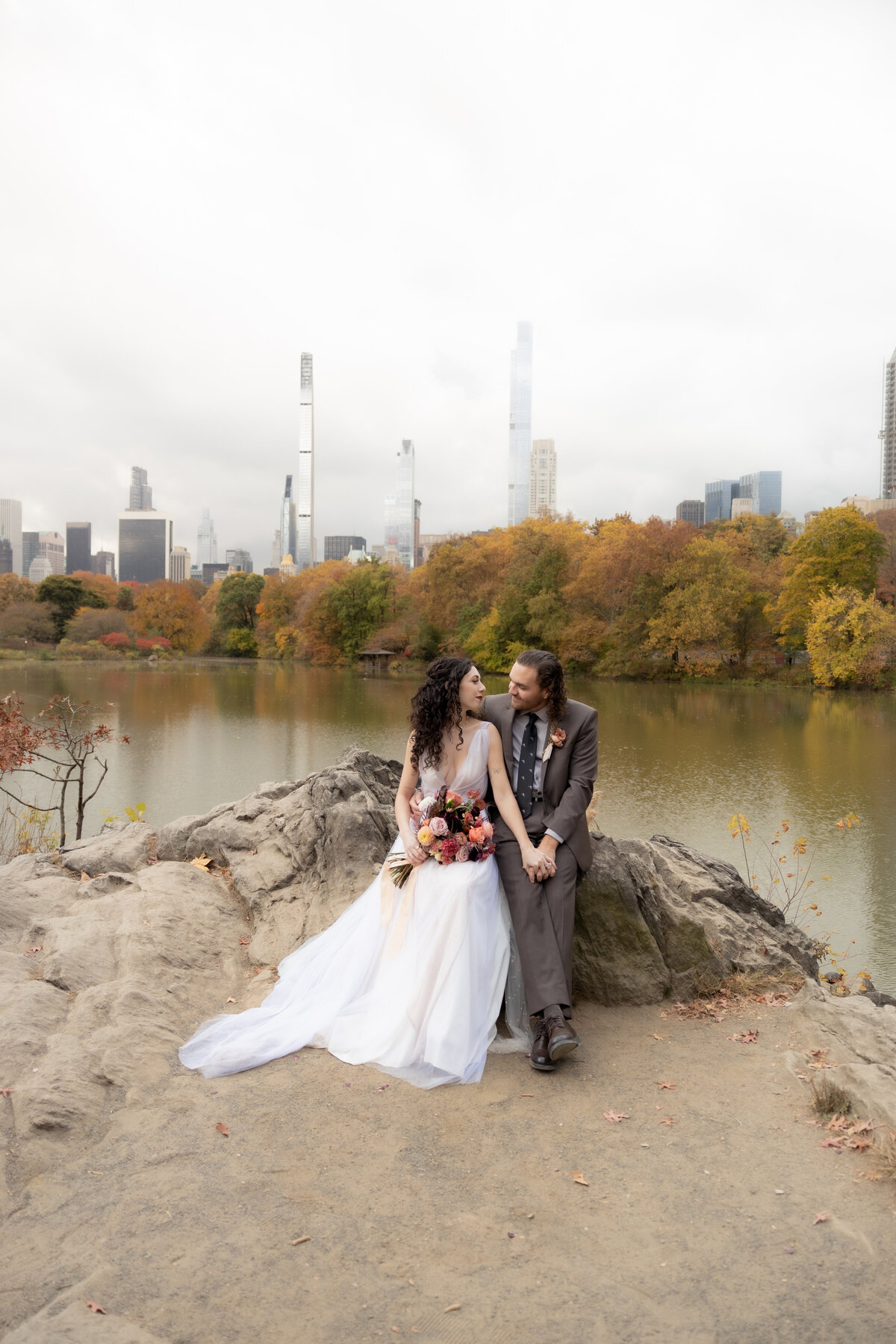 The couple standing close together surrounded by Central Park’s glowing fall foliage.