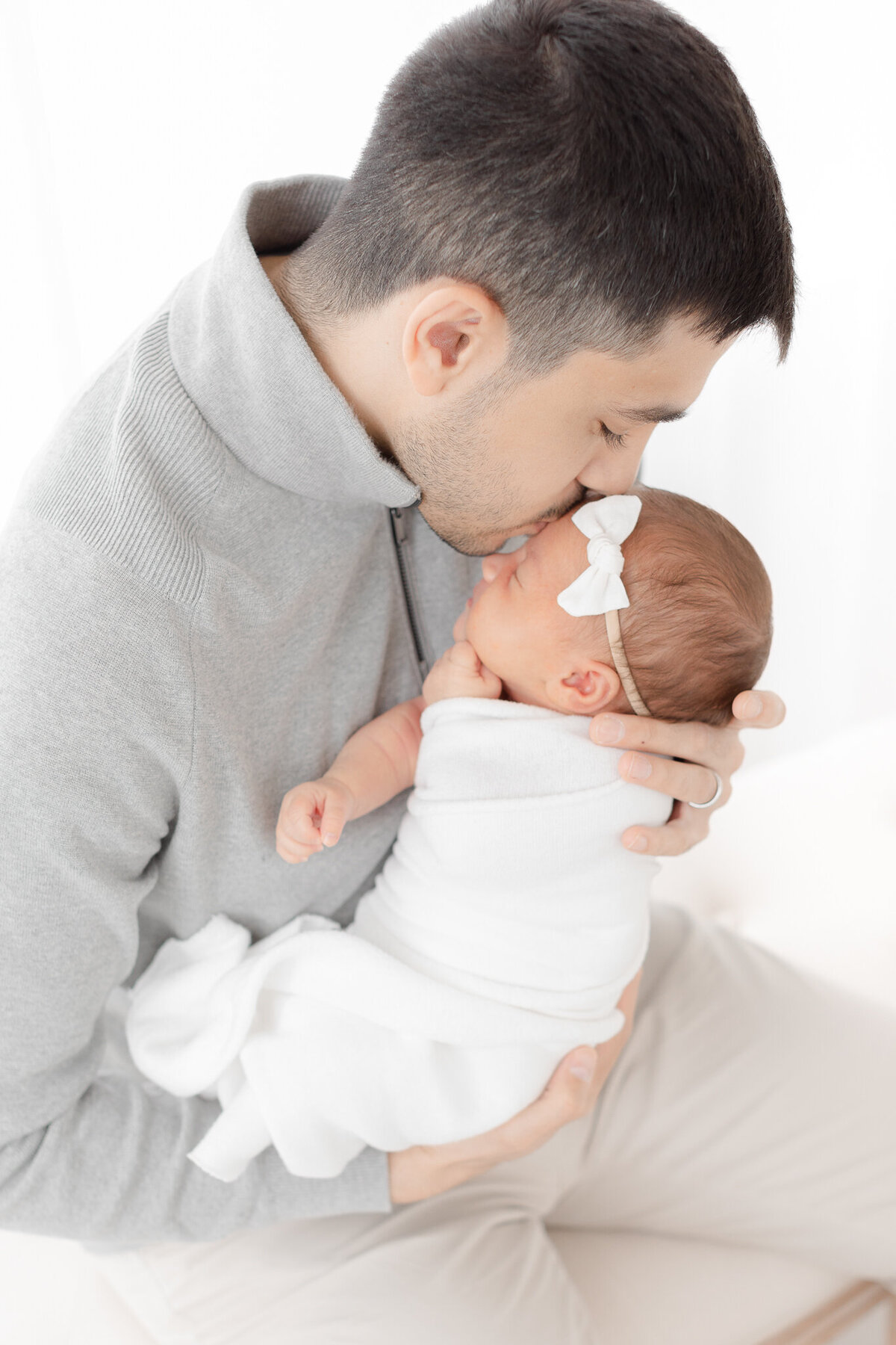 dad holds newborn and leans down for forehead kiss taken by boston newborn photographer