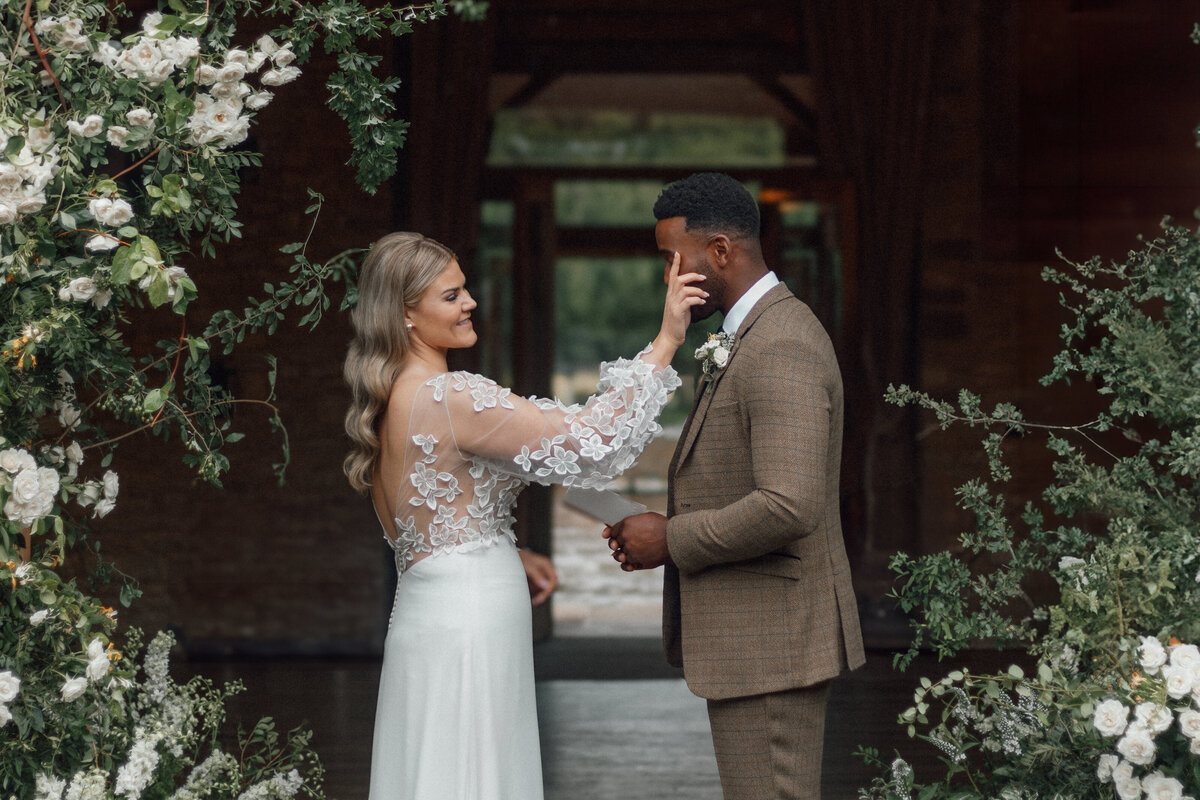 Wedding photographer captures the moment a new bride wipes away the tears from her husband in a rustic barn ceremony.