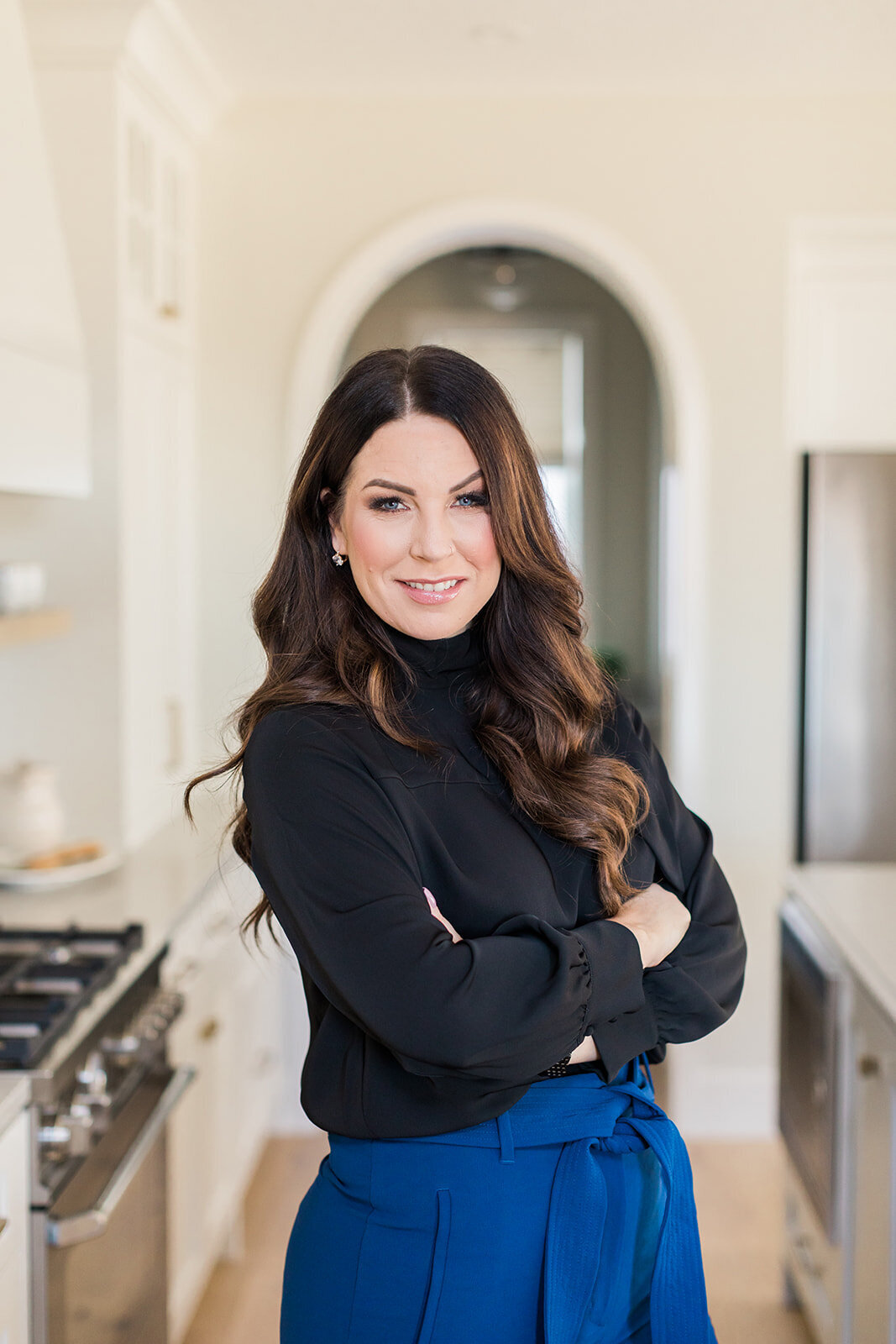Brand headshot of Calgary business woman with dark hair crossing her arms in a modern kitchen.