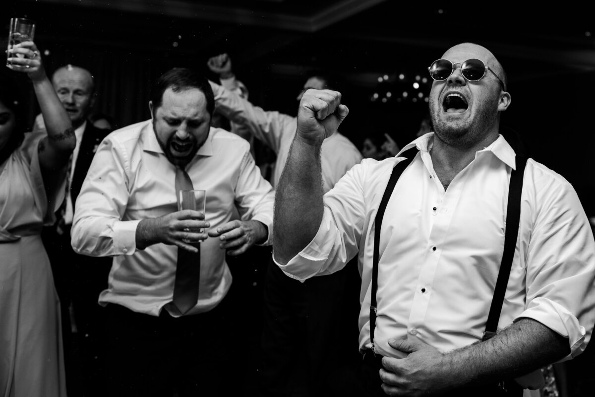 Black and white photograph of groomsmen dancing at a wedding.