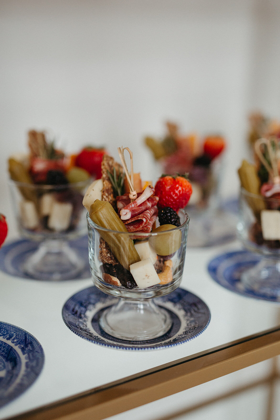 Charcuterie hors d’oeuvres in a glass cup atop blue and white plates set on a counter.