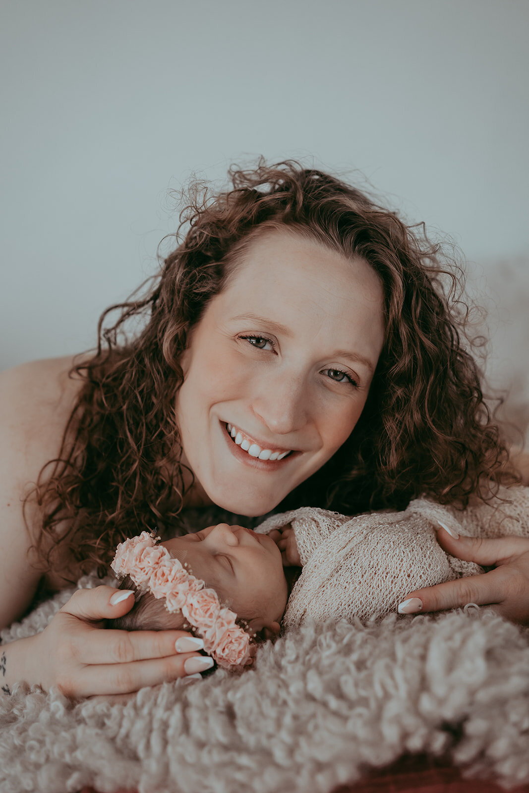 mother of a newborn smiles while laying next to her infant daughter