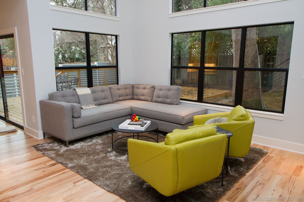 mid century modern furniture paired with a large area rug in a living room with tall ceilings and large windows.